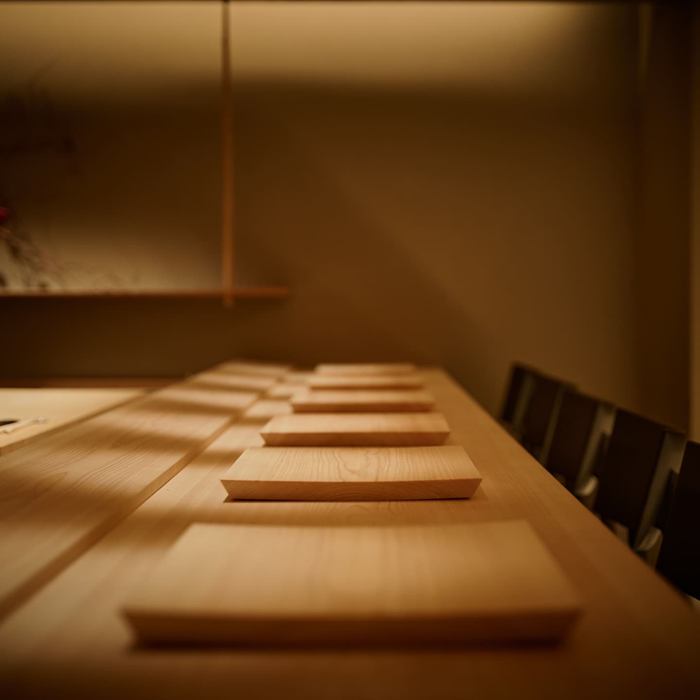 Alt設定値： 白木のカウンターが奥へと続く高級和食店の内観、職人の舞台と客席の境界を美しい陰影で捉えた空間撮影