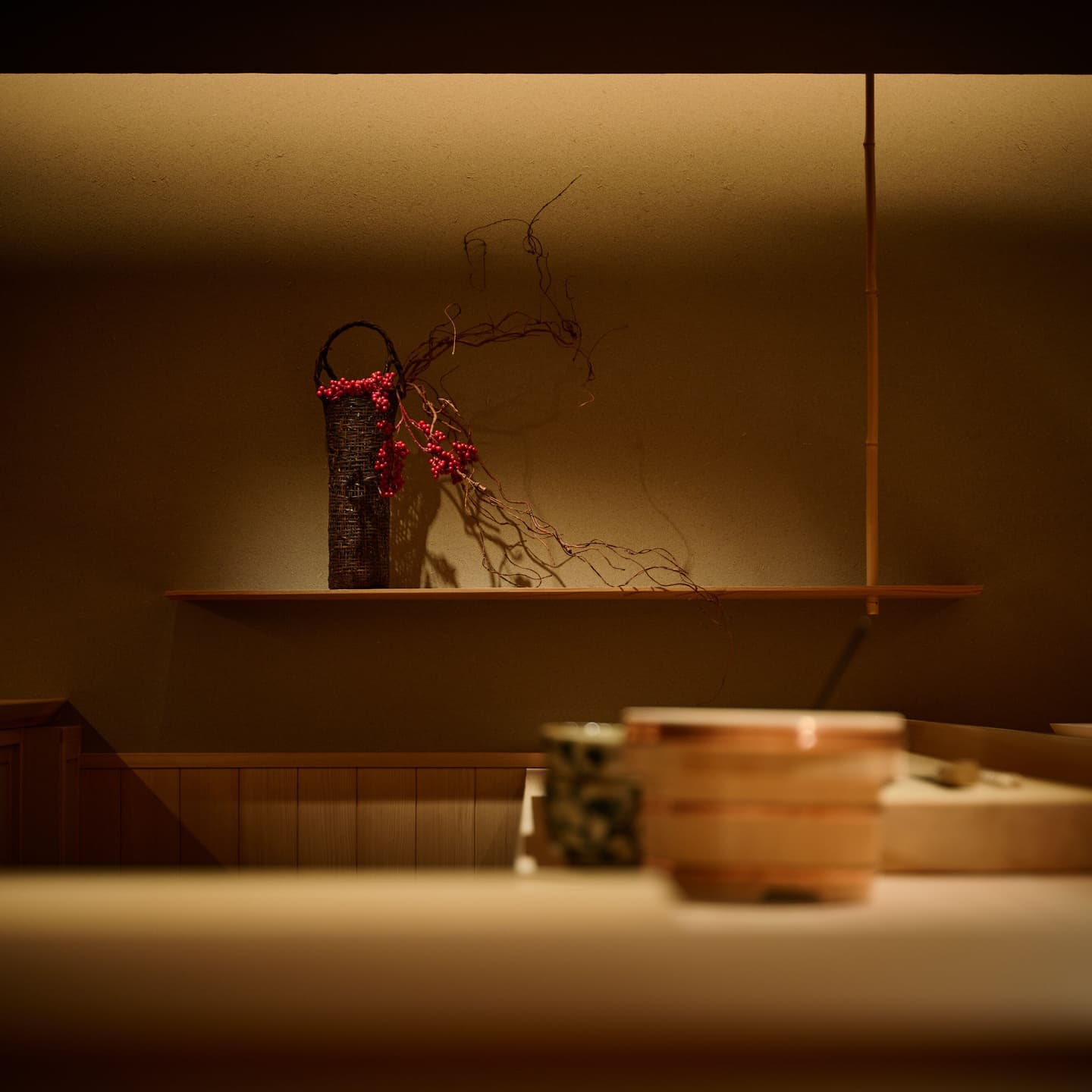 Alt設定値：高級和食店のカウンター奥に飾られた季節の生け花、陰影の中に浮かび上がる繊細な意匠と店内の静謐な空気感
