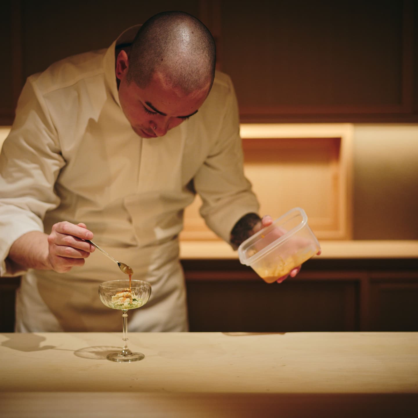 繊細な手つきでデザートを仕上げる料理人の所作、真剣な眼差しと静謐な厨房の空気感を切り取ったライブ感のあるポートレート撮影