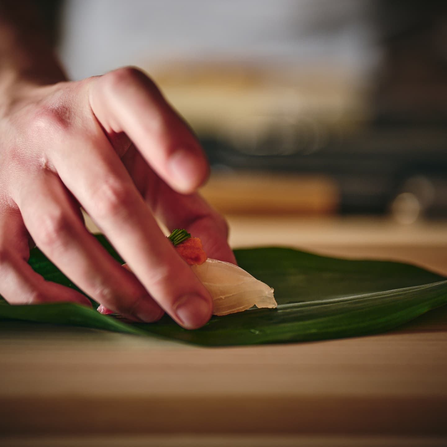 笹の葉に握り鮨を静かに置く職人の指先のクローズアップ、一貫に魂を込める緊張感と美しい所作を捉えたマクロ撮影
