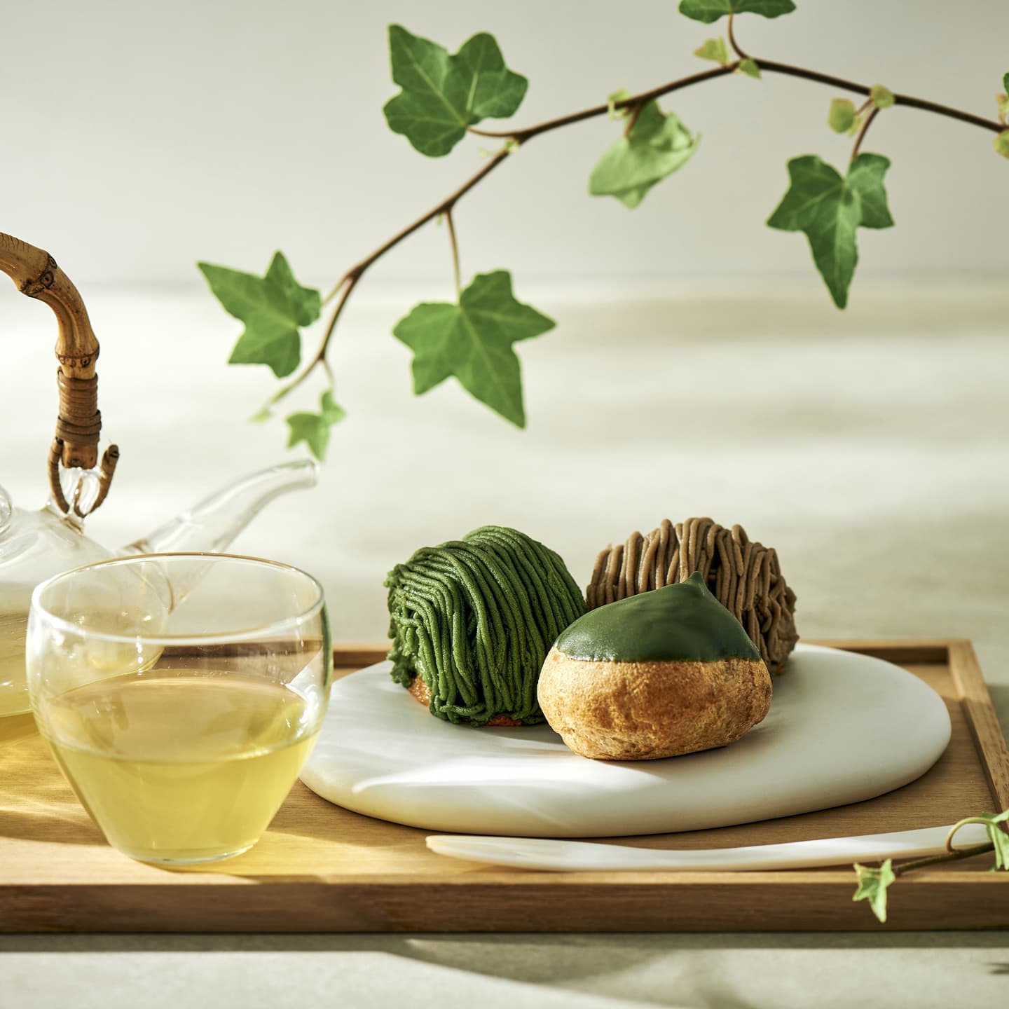 竹製の持ち手の急須や透明な茶器、アイビーの枝葉を配した和洋折衷のスイーツ撮影。プロップスによって清涼感と静謐な空気感を演出し、商品の繊細な表情を引き出したフードビジュアル