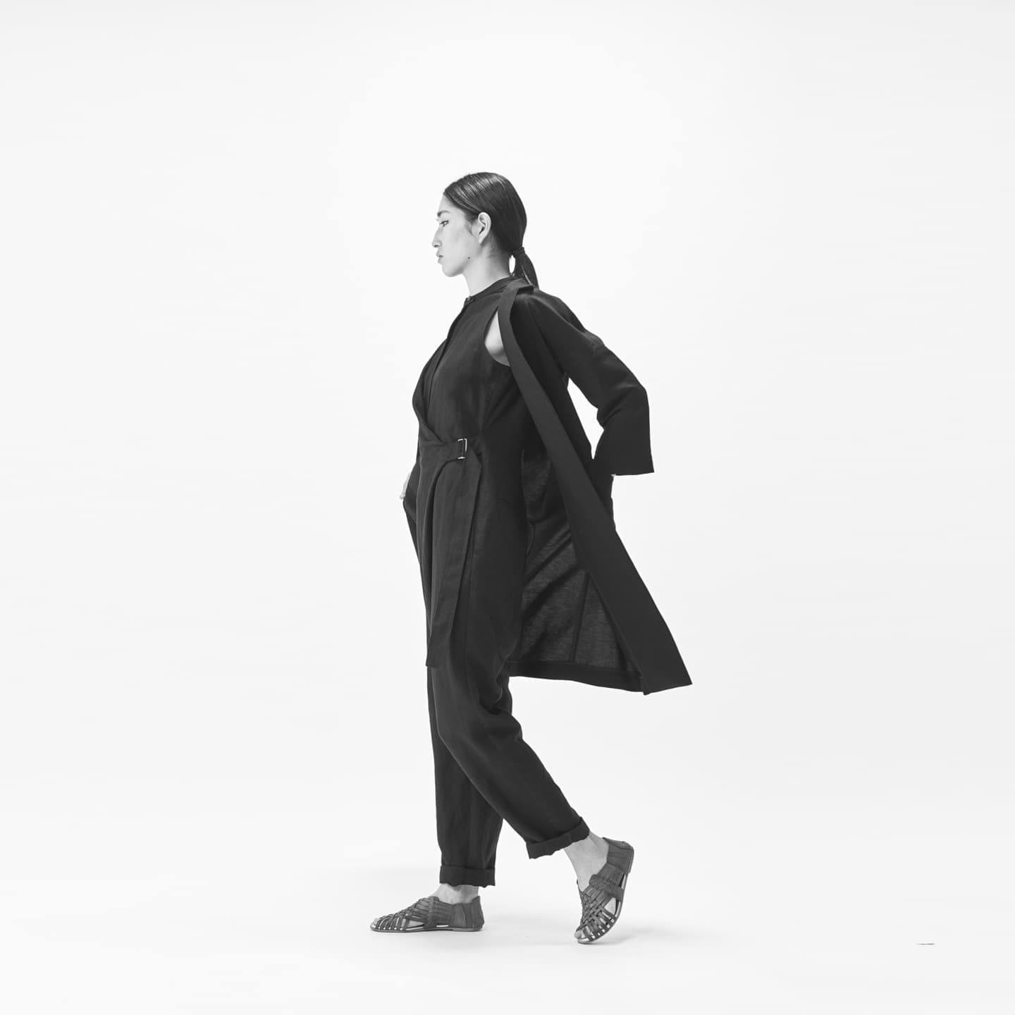 凛とした表情で前を見据え、コートを羽織る女性のモノクロポートレート。ブランドの意志を体現する、躍動感と品格のある全身ショット。