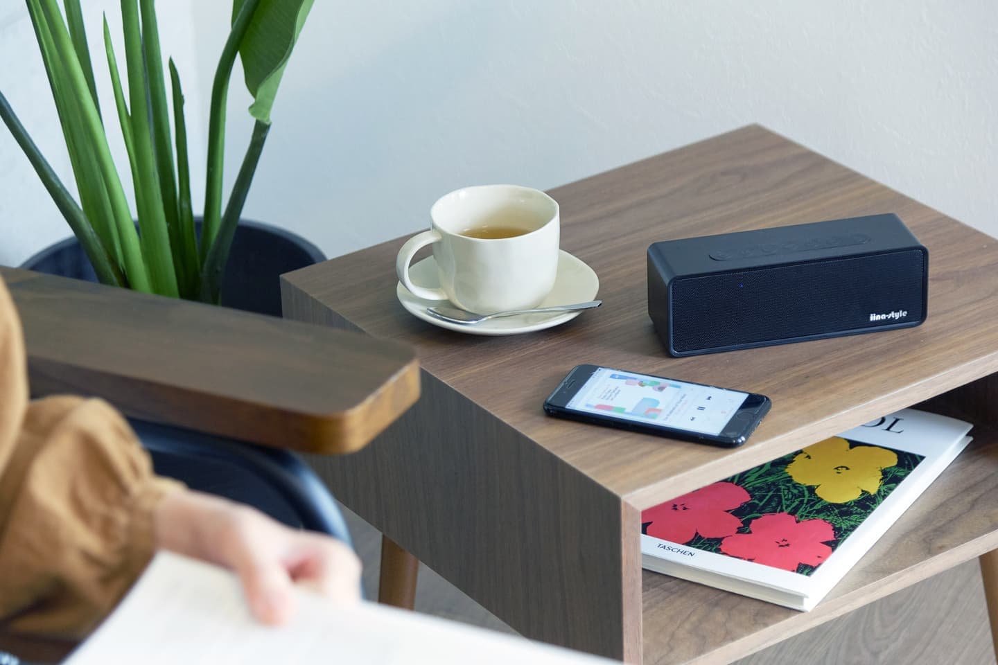 大阪のスタジオで撮影された、午後のティータイム。木製サイドテーブルに置かれた黒のワイヤレススピーカーとカップ、雑誌。音楽とともに過ごす上質な日常を演出したブランドビジュアル。