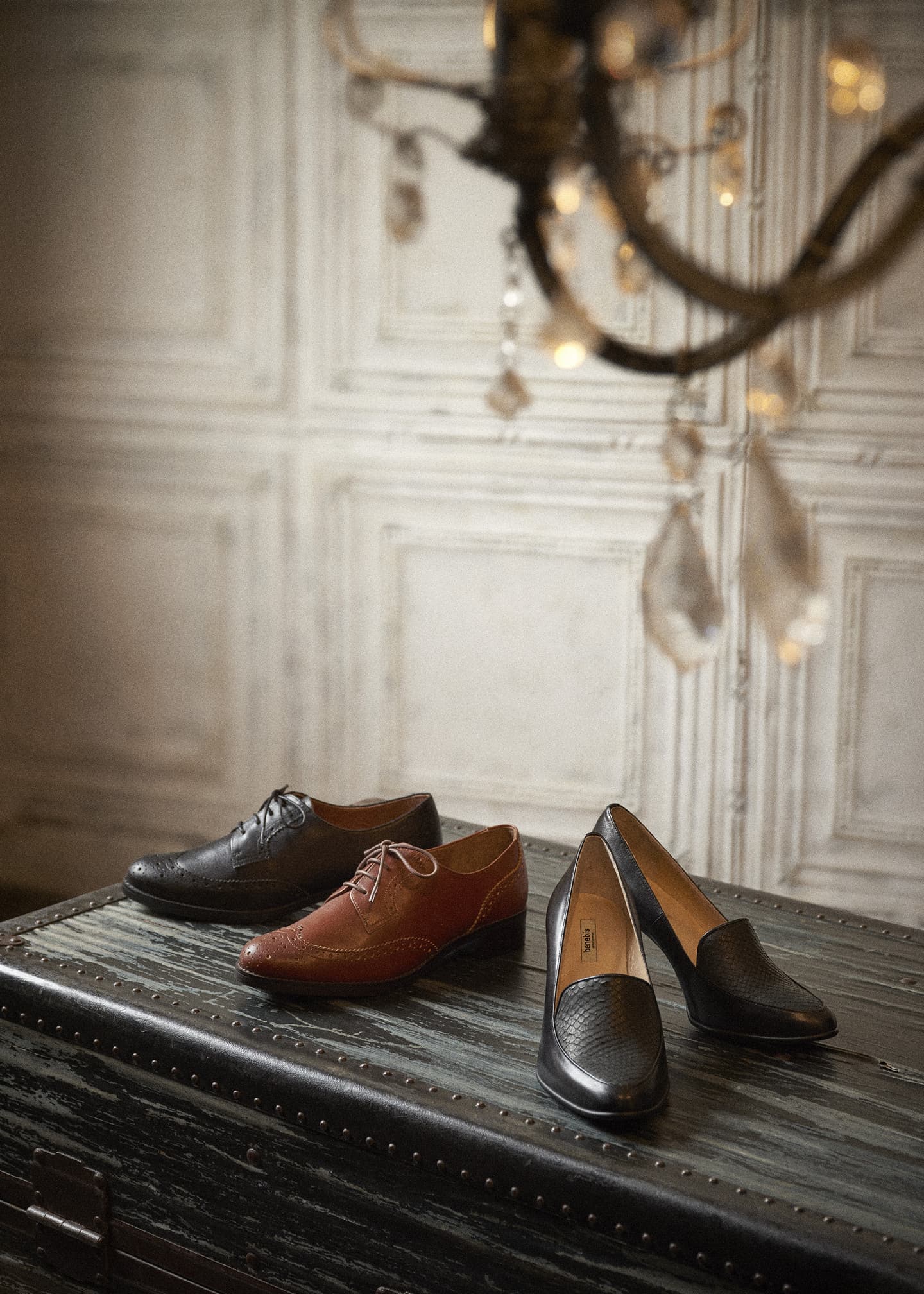 大阪のスタジオで撮影された、アンティークトランクとシャンデリアが彩る重厚な室内。クラシックな革靴を配し、ブランドの伝統と上質さを演出した情緒的な商品スタイリング写真。